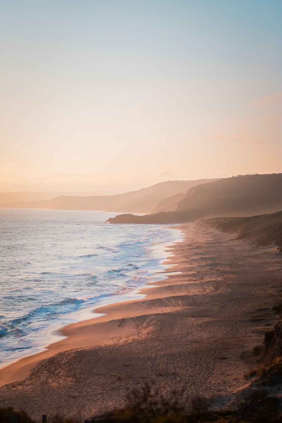 Waves roll onto a sandy beach near coastal cliffs.